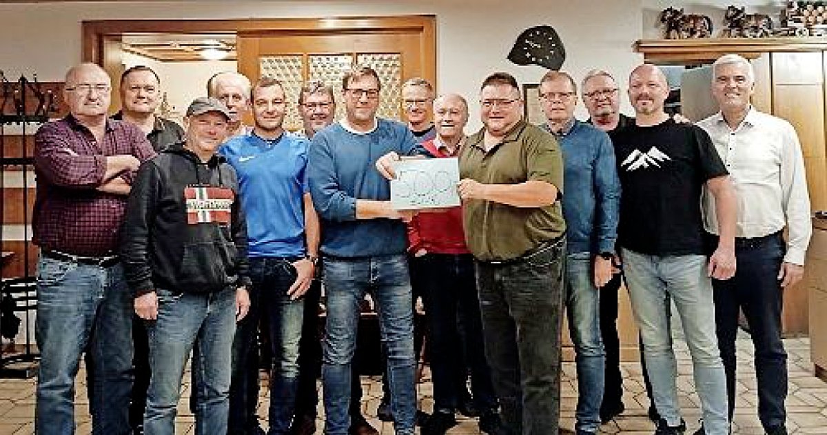 Eine Gruppe Männer in Freizeitkleidung stehen in einem Innenraum in einer Gruppe. Zwei Männer in der vorderen Reihe halten gemeinsam ein Schild. Darauf steht 500 Euro. Alle lächeln in die Kamera.