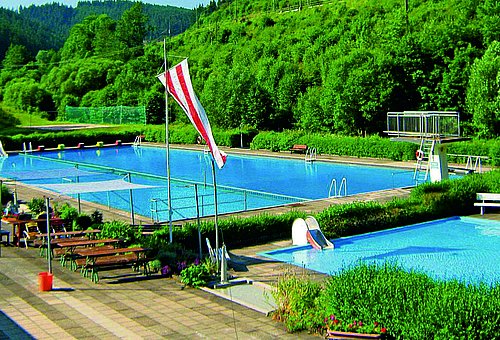 Das Freibad mit einem großen Schwimmerbecken und einem Kleinkindbecken. Umrahmt ist das Bad von dichten Wäldern. 