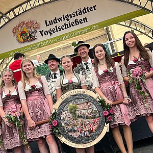 Schützenkönig und Jungschützenkönig. Davor sieben Schützenliesel in Dirndl. Zwei davon halten die Königsscheibe von Schützenkönig Florian Bauer.