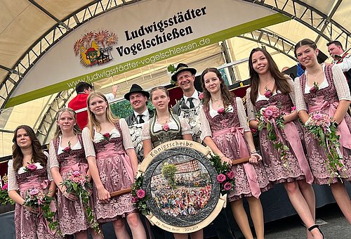 Schützenkönig und Jungschützenkönig. Davor sieben Schützenliesel in Dirndl. Zwei davon halten die Königsscheibe von Schützenkönig Florian Bauer. 