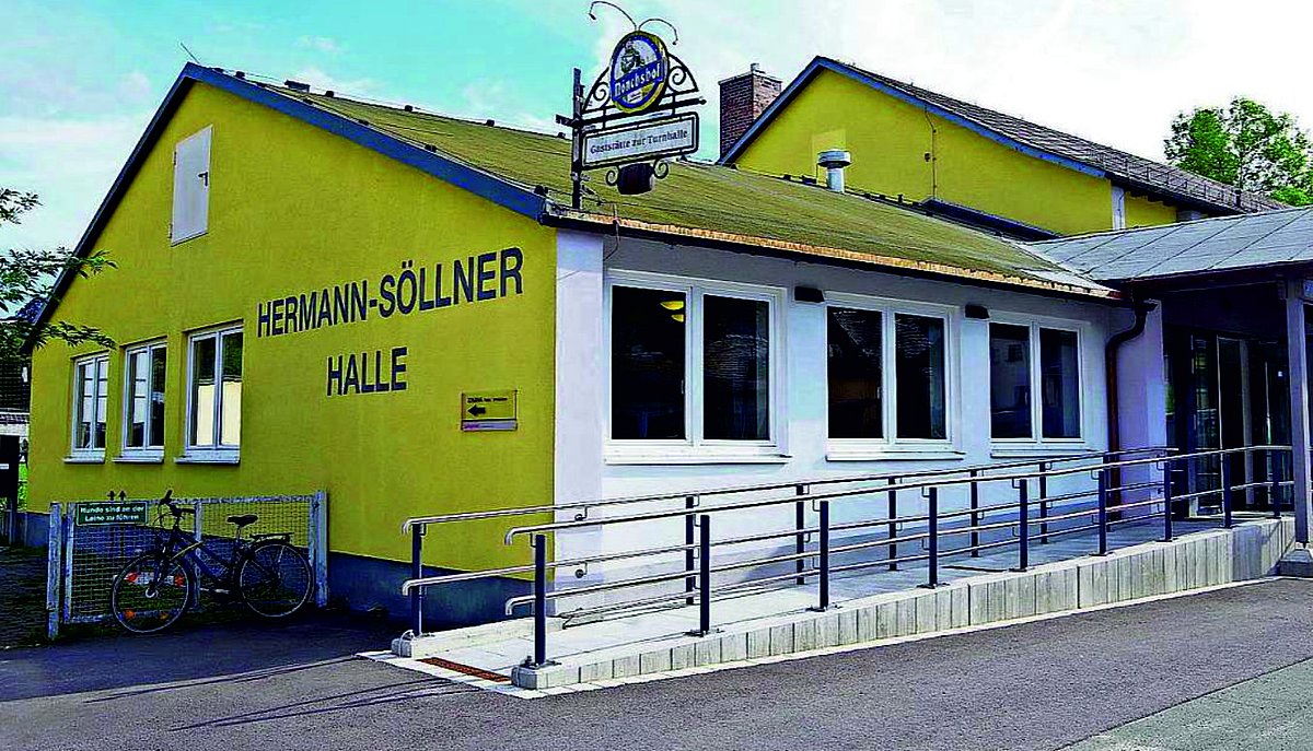 Zu sehen ist die neu gestaltete Hermann-Söllner-Halle. Die Front strahlt in einem hellen Gelb mit Schriftzug Hermann-Söllner-Halle. Rechts davon ist der barrierefreie Zugang zur Halle.