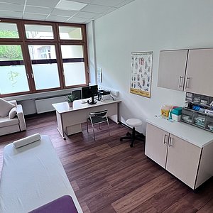 Auf dem Foto ist ein Behandlungszimmer mit Liege, Schreibtisch und Schrank zu sehen.