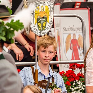 Das Foto zeigt einen Jungen, der das Schild der Ludwigsstädter Schützen trägt. Das Schild zeigt das Wappen der Schützengesellschaft. Der Junge schaut ganz konzentriert und trägt ein blau-weiß kariertes Hemd und eine Lederhose.