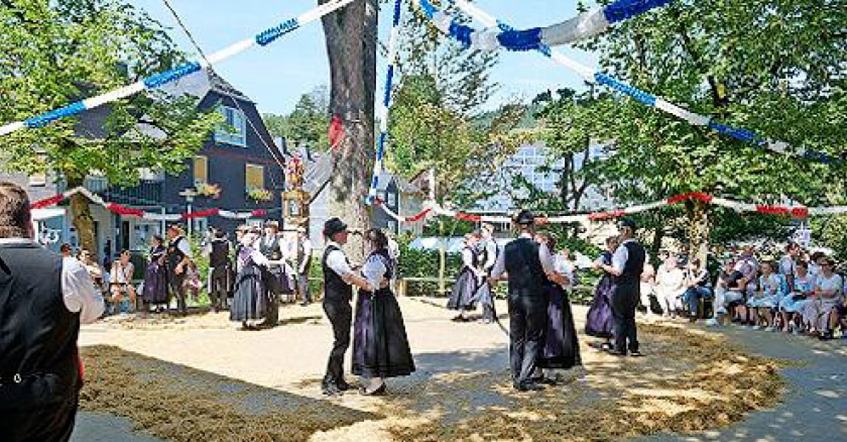 Tanzpaare in historischen Trachten tanzen auf einem Platz, der mit Stroh bedeckt ist. Zuschauer stehen im Kreis drumherum.
