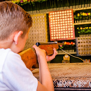 Das Bild zeigt einen Jungen, der mit einem Luftgewehr auf die Ziele in der Schießbude zielt.