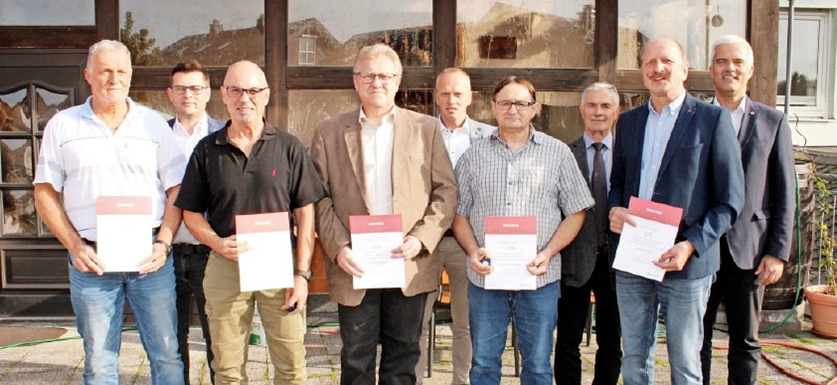 Eine Gruppe von Menschen schauen in die Kamera. Sie stehen in zwei Reihen hintereinander. Die Personen in der vorderen Reihe halten je eine Urkunde in der Hand. Sie alle lächeln.