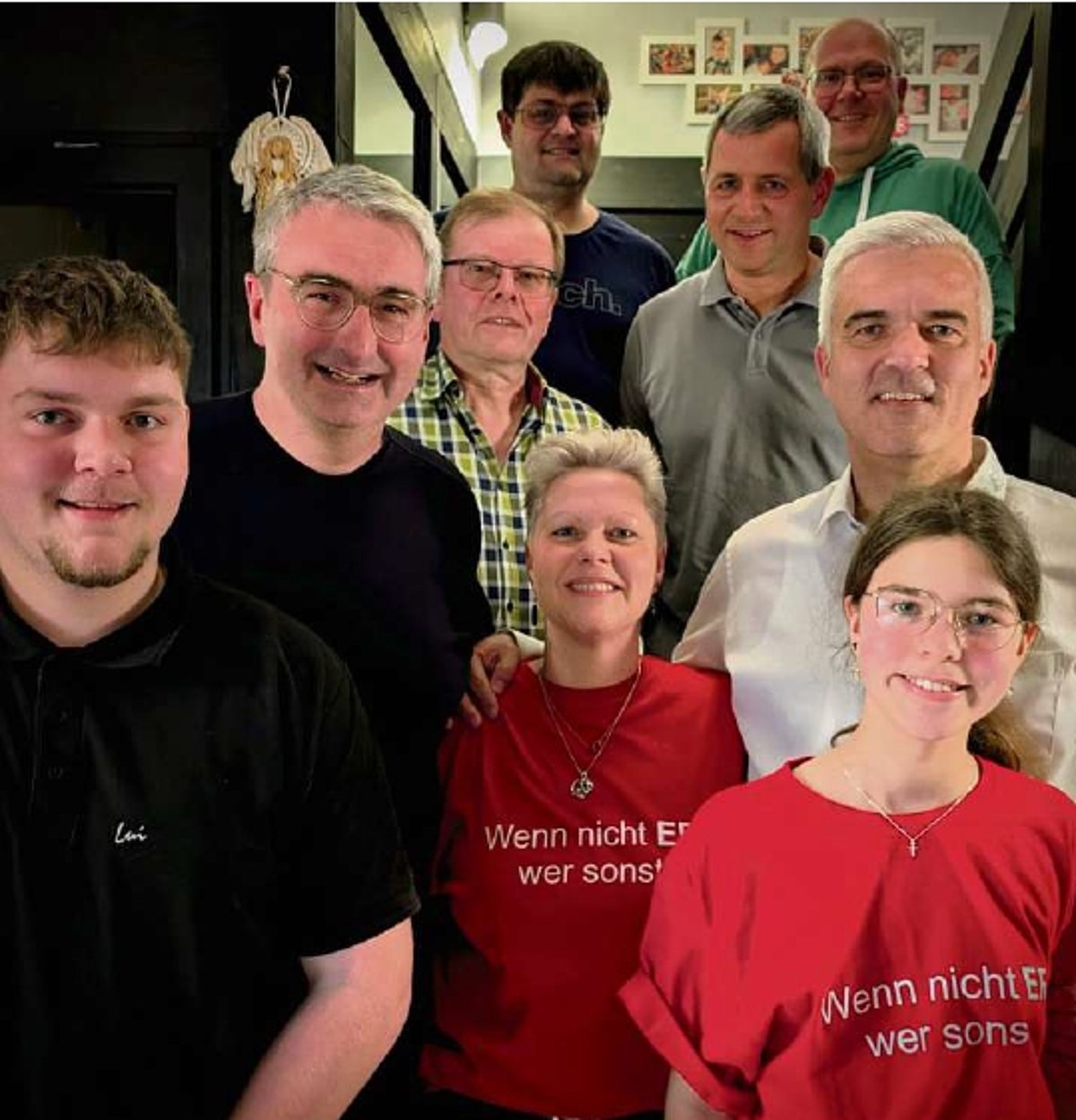 Auf einer Treppe in einem Gebäude steht eine kleine Gruppe von Menschen. Darunter sieben Männer und zwei Frauen. Alle tragen Freizeitkleidung und lächeln in die Kamera.