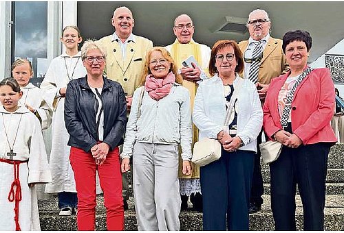 Eine Gruppe von Menschen, darunter drei Kinder in weißer Kleidung und 7 erwachsene Menschen. Sie alle lächeln in die Kamera.