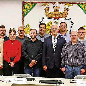 In einem Raum vor einer bemalten Wand steht eine Gruppe von Menschen, darunter zwei Frauen. Sie alle lächeln in die Kamera.