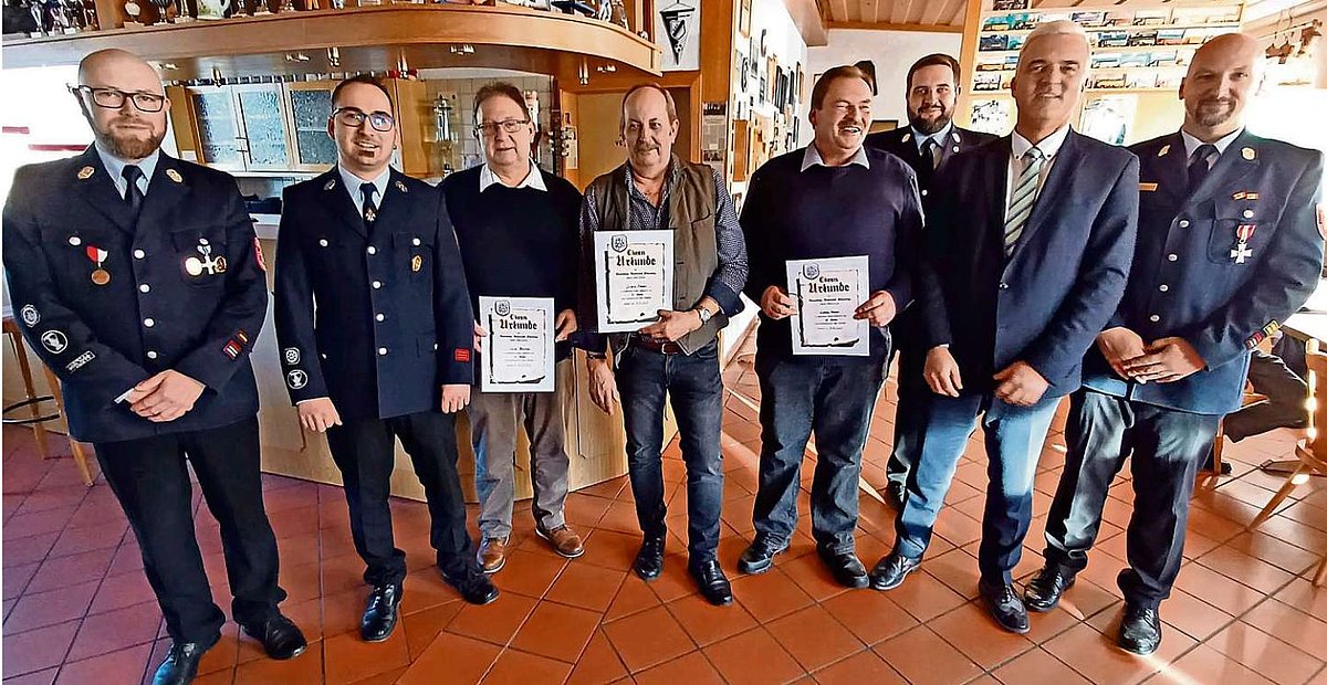 Auf dem Foto ist eine Gruppe von Männern zu sehen, teils mit Feuerwehruniform. In der Mitte stehen drei mit Urkunde, die für jahrelange Vereinstreue geehrt wurden.