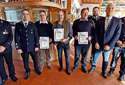 Auf dem Foto ist eine Gruppe von Männern zu sehen, teils mit Feuerwehruniform. In der Mitte stehen drei mit Urkunde, die für jahrelange Vereinstreue geehrt wurden.