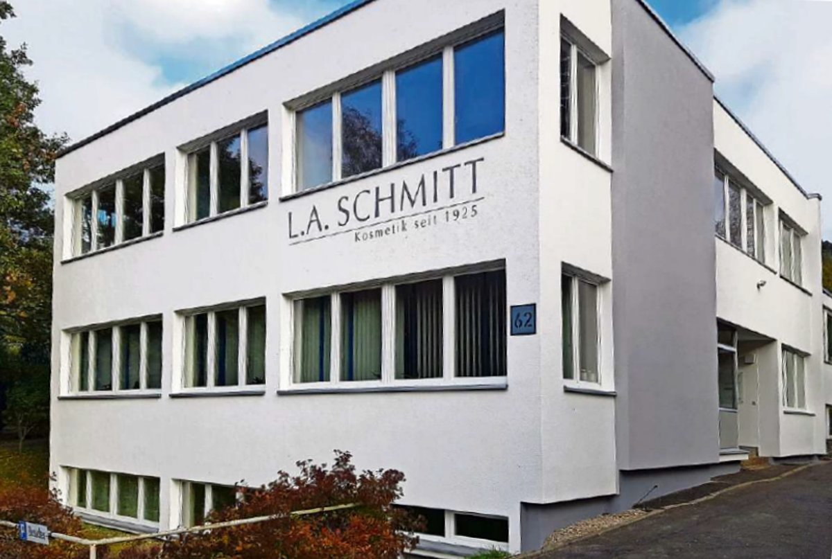 Ein modern wirkendes Gebäude in weiß mit grauen Akzenten. Es hat große Fenster und einen Schriftzug : L.A.Schmitt, Kosmetik seit 1925.