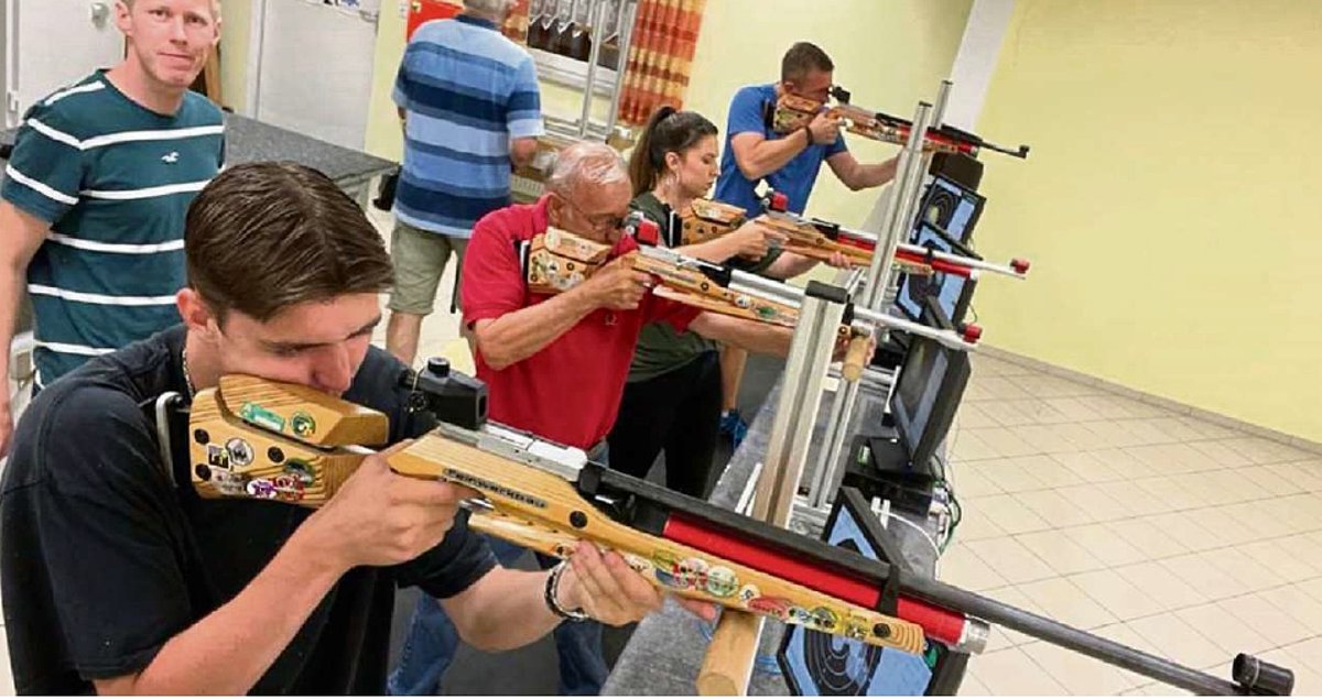 Männer und Frauen in Freizeitkleidung stehen und halten ein Luftgewehr im Anschlag.