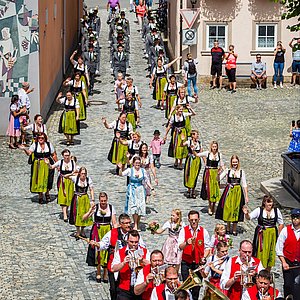 Hinter der Ebersdorfer Blaskapelle laufen die Schützendamen in ihren prächtigen Trachten. Diese bestehen aus weißen Blusen, langen schwarzen Röcken und intensiv grünen Schürzen mit verschieden farbigen Bändern.