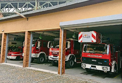 Ein Gebäude mit vier großen Toren. Durch diese kann man die Feuerwehrfahrzeuge stehen sehen.
