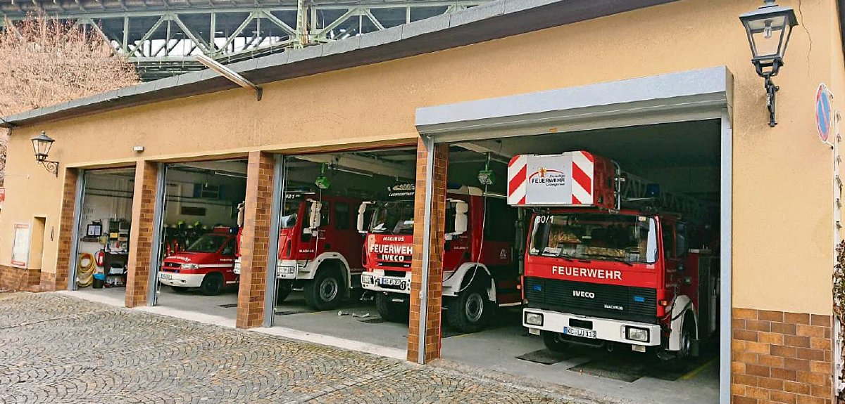 Ein Gebäude mit vier großen Toren. Durch diese kann man die Feuerwehrfahrzeuge stehen sehen.