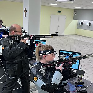 Zu sehen sind Schützen an einem Schießstand. Sie stehen konzentriert und sind gerade beim schießen.