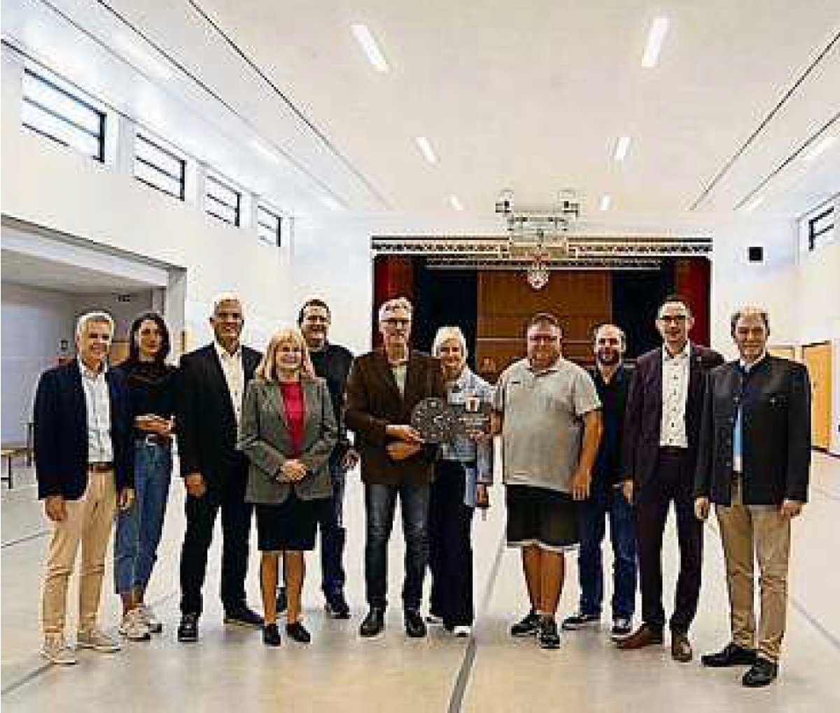 In einer hellen großen Halle steht eine Gruppe von Menschen beieinander. Sie alle lächeln in die Kamera.
