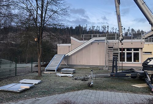 An einem Haus wird eine neue Fluchtwegtreppe mit einem Kran angebaut. 