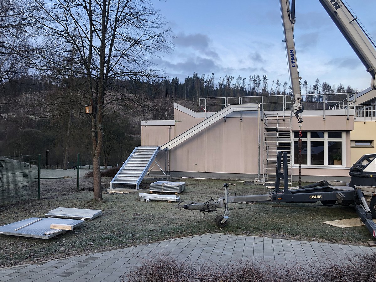 An einem Haus wird eine neue Fluchtwegtreppe mit einem Kran angebaut.