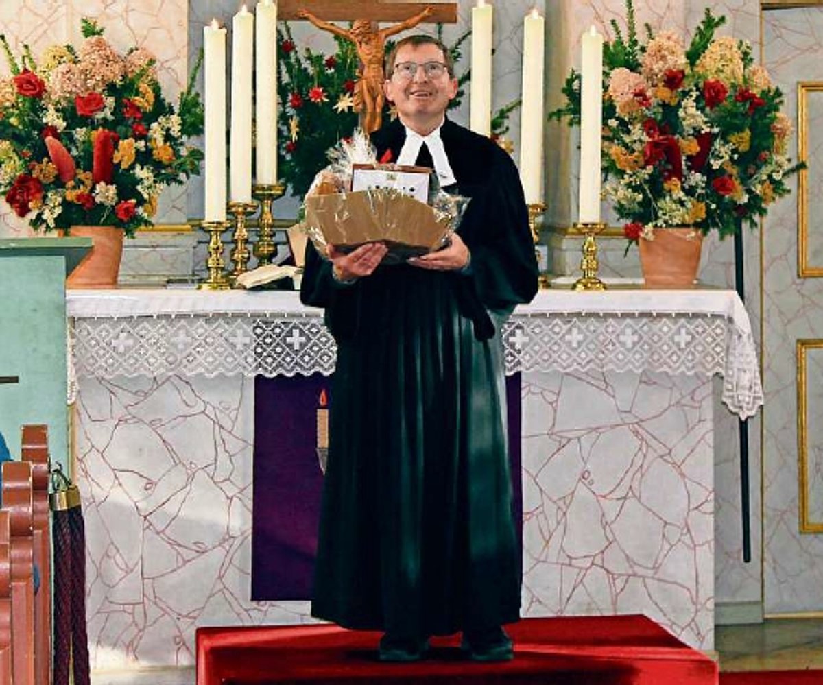 Ein älterer Mann im Talar steht mit einem Geschenkkorb vor dem Altar in einer Kirche.