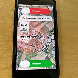 Das Bild zeigt ein Smartphone. Auf dem Bildschirm ist eine APP zusehen mit einer Karte und einem Button in grün für Annehmen und einem Button in rot für Ablehnen.