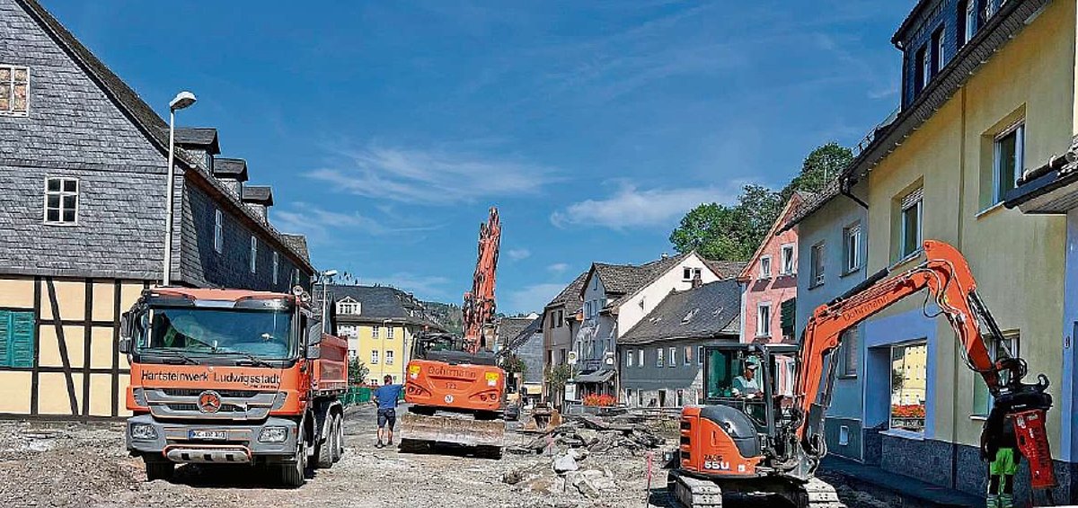 Eine aufgegrabene Straße mit Wohnhäusern rechts und links. Im Baustellenbereich stehen Baustellenfahrzeuge.