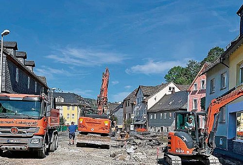 Eine aufgegrabene Straße mit Wohnhäusern rechts und links. Im Baustellenbereich stehen Baustellenfahrzeuge.