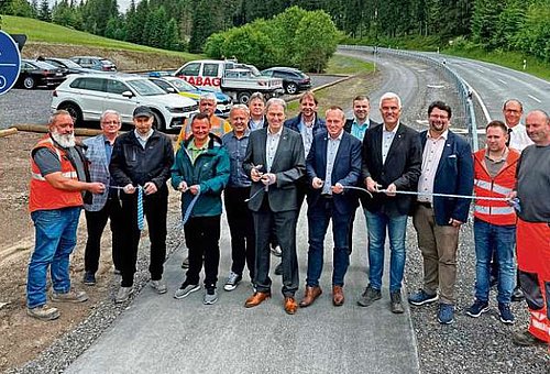 Das Foto zeigt eine Gruppe von Männern, die auf einem neu geteerten Radweg ein Band zerschnitten haben, für die Freigabe des Weges.
