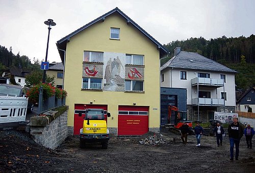 Das Feuerwehrgebäude in Lauenstein und ein weiteres Wohnhaus. Die Aspaltbereiche davor sind aufgegraben. Personen schauen sich diese Baustelle an. 