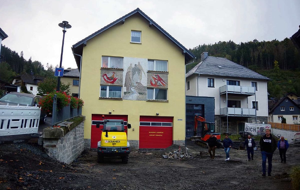 Das Feuerwehrgebäude in Lauenstein und ein weiteres Wohnhaus. Die Aspaltbereiche davor sind aufgegraben. Personen schauen sich diese Baustelle an. 