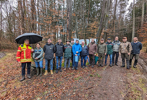 Eine große Gruppe von Menschen stehen vor einem herbstlichen Wald im Regen.