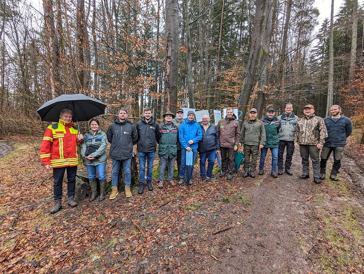 Eine große Gruppe von Menschen stehen vor einem herbstlichen Wald im Regen.