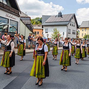 Das Foto zeigt die Frauen der Schützen in ihren Trachten; weiße Blusen, schwarze lange Röcke und grüne Schürzen. Sie laufen im Festumzug durch die Stadt.