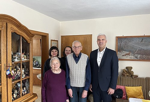 Das Gbeurtstagskind mit seiner Frau auf der linken Seite und Bürgermeister Timo Ehrhardt an seiner anderen Seite. Dahinter stehen zwei Frauen. Sie alle lächeln in die Kamera.