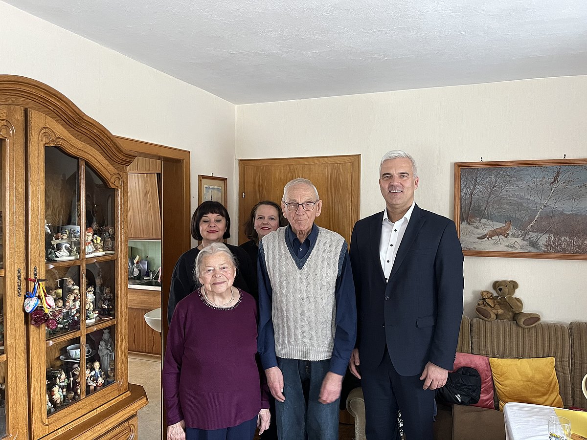 Das Gbeurtstagskind mit seiner Frau auf der linken Seite und Bürgermeister Timo Ehrhardt an seiner anderen Seite. Dahinter stehen zwei Frauen. Sie alle lächeln in die Kamera.